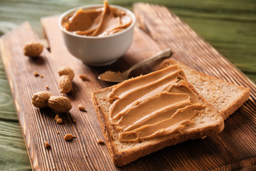 Toasted bread with tasty peanut butter on wooden board