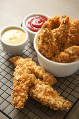 Cooling rack with tasty nuggets and sauces on grey table