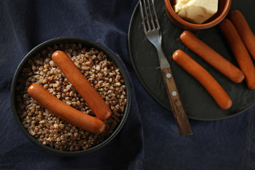 Bowl with tasty boiled buckwheat, sausages and butter on table