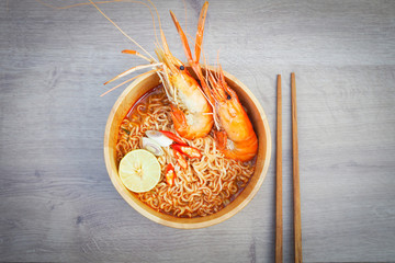 Spicy instant noodles soup with shrimp in wooden bowl on wood background,Tom yum kung