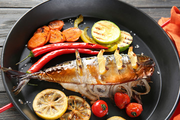 Frying pan with tasty mackerel fish and vegetables on table