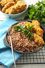 Frying pan with tasty boiled buckwheat and nuggets on table