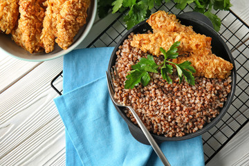 Frying pan with tasty boiled buckwheat and nuggets on table