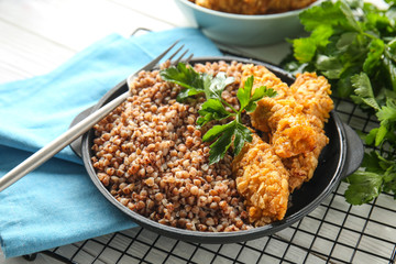 Frying pan with tasty boiled buckwheat and nuggets on table