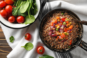 Frying pan with tasty boiled buckwheat and vegetables on table