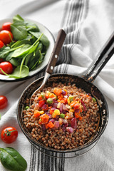 Frying pan with tasty boiled buckwheat and vegetables on table
