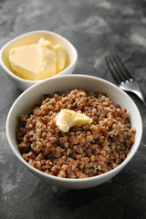 Bowl with tasty boiled buckwheat and butter on grey table
