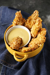 Pot with tasty nuggets and cheese sauce on grey table