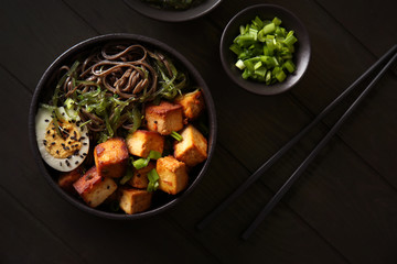 Bowl with tasty fried tofu cheese and soba noodles on table
