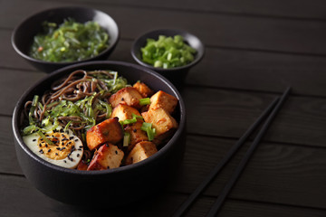 Bowl with tasty fried tofu cheese and soba noodles on table
