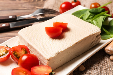 Plate with tasty tofu cheese and tomatoes on wooden table