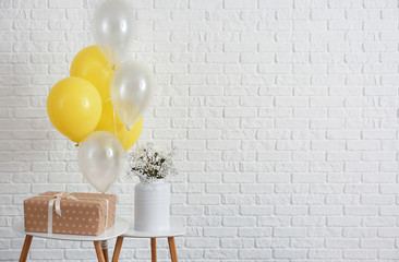 Table with gift box and balloons on white brick background
