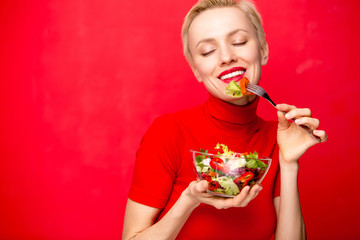 Beautiful caucasian woman eating salad over red background	