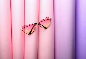 Heart-shaped sunglasses on color background