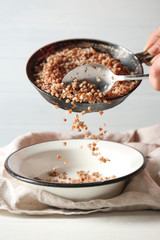 Pouring of tasty buckwheat from frying pan into bowl on table