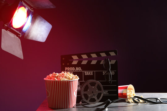 Movie clapper with film reel, popcorn and glasses on table