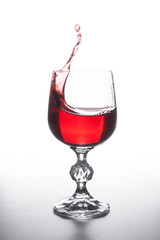 Red wine splashing in wine glass on light background. .