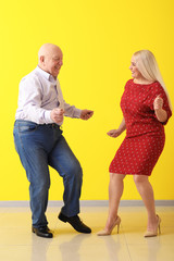 Cute elderly couple dancing near color wall