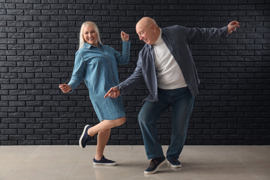 Cute Elderly Couple Dancing Against Dark Brick Wall