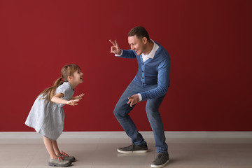 Father and his cute little daughter dancing near color wall