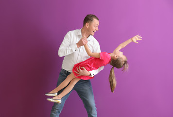 Father and his cute little daughter dancing near color wall