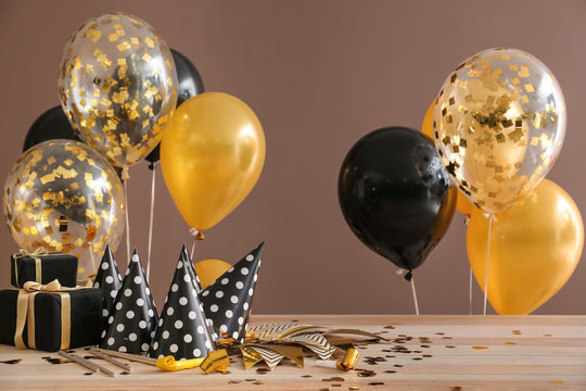 Balloons, gifts and party hats on table against color background