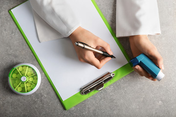 Doctor writing out prescription for using inhaler against asthma