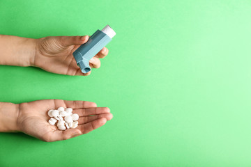 Female hands with inhaler and pills against asthma on color background