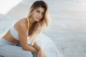 Attractive millennial woman runner taking break sitting stairs watching sunset, exercising, jogging...
