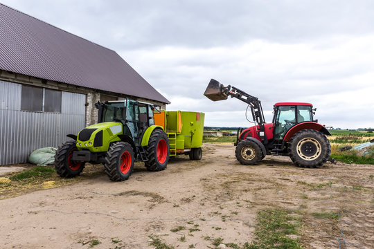 Tractor with front end loader loads the food into a distributor of animal feed for cows. Necessary equipment for a dairy farm.