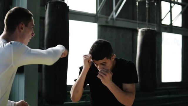 Two boxers skillfully work out punches. Shy away from blows protecting the face. Boxing training together in old style gy. Boxing bags on the background. Slow motion