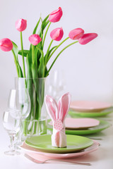 Happy easter. Decor and table setting of the Easter table is a vase with pink tulips and dishes of pink and green color.