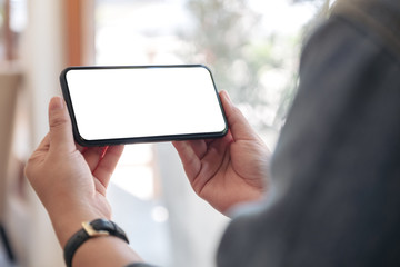 Mockup image of hands holding black mobile phone with blank desktop screen horizontally in cafe