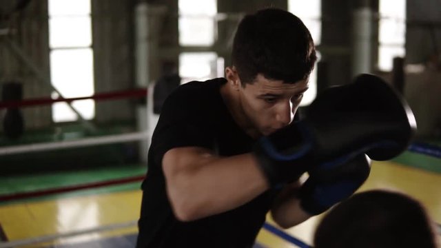 Rare view of determinated male boxers on the ring at gym fulfills punches with each other and ways how to skip hits. Men train strikes, protection and reactions. Slow motion