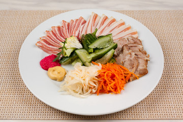Meat and lard with vegetables on a white plate on the table.