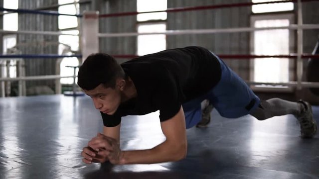 Close up of young muscular sportsman doing push-ups - from elbows to outstretched hands - while working out in boxing gym