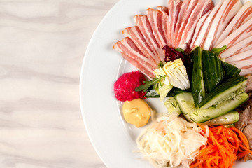 Meat and lard with vegetables on a white plate on the table.