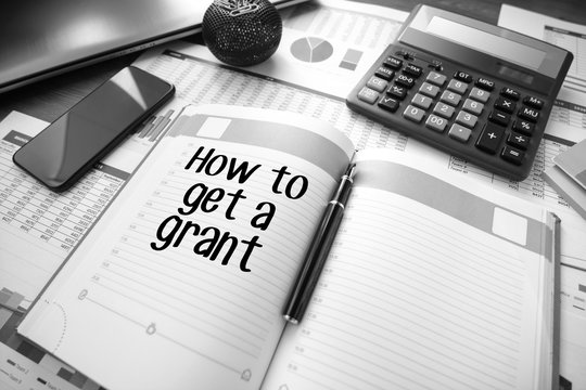 Business accessories, smartphone calculator, laptop, reports and diary with text How to get a grant