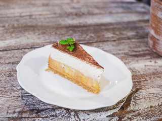Close up banoffee pie with bananas, whipped cream, caramel, coffee and toffee on the white plate isolate wood background.