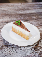 Close up banoffee pie with bananas, whipped cream, caramel, coffee and toffee on the white plate isolate wood background.