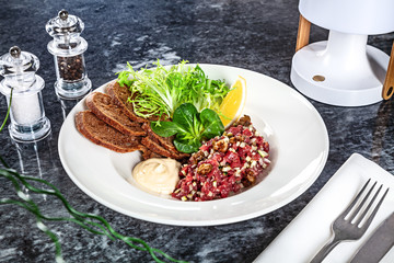 Close up view on served Steak beef tartare served with lemon, bread, sauce and salad on marble table. Restaurant food menu, recipe photo with copy space