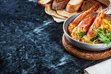 Close up view on shrimps in pan on marble table. Seafood with green and bread. Restaurant food menu, recipe photo with copy space