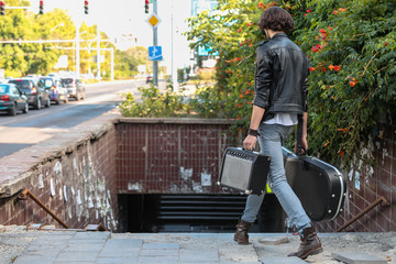 Street musician holding a case with a guitar and amplifier. Descends into the underground passage. Vagrant lifestyle. Playing to make money a living. Unemployed musician. Future rock star.