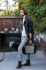 Street musician holding a case with a guitar and amplifier. Descends into the underground passage. Vagrant lifestyle. Playing to make money a living. Unemployed musician. Future rock star.