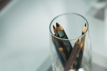 Glass Cup with brown and black pencils on the glass table. Close up. Copy space.