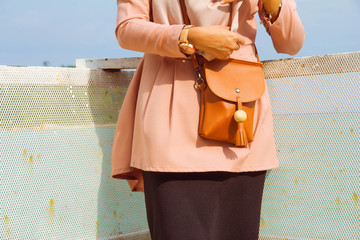 Young woman donning outreach colour dress with leather sling bag. Faceless. 