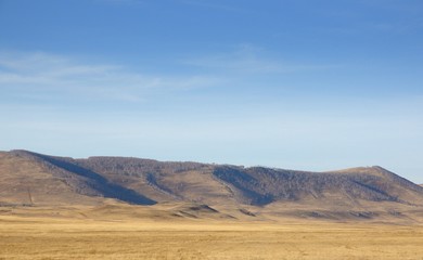 Smooth hills covered with dry grass on horizon with blue sky in Khakassia, Russia