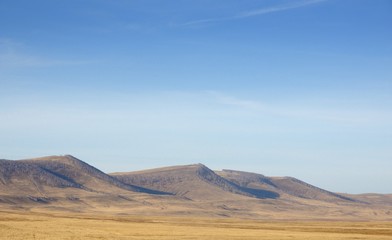 Fototapeta na wymiar Smooth hills covered with dry grass on horizon with blue sky in Khakassia, Russia