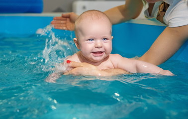 Fototapeta na wymiar Baby in pool bathing health procedures with mother hands swimming