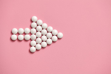 Arrow sign is lined with white, round tablets on a pink background